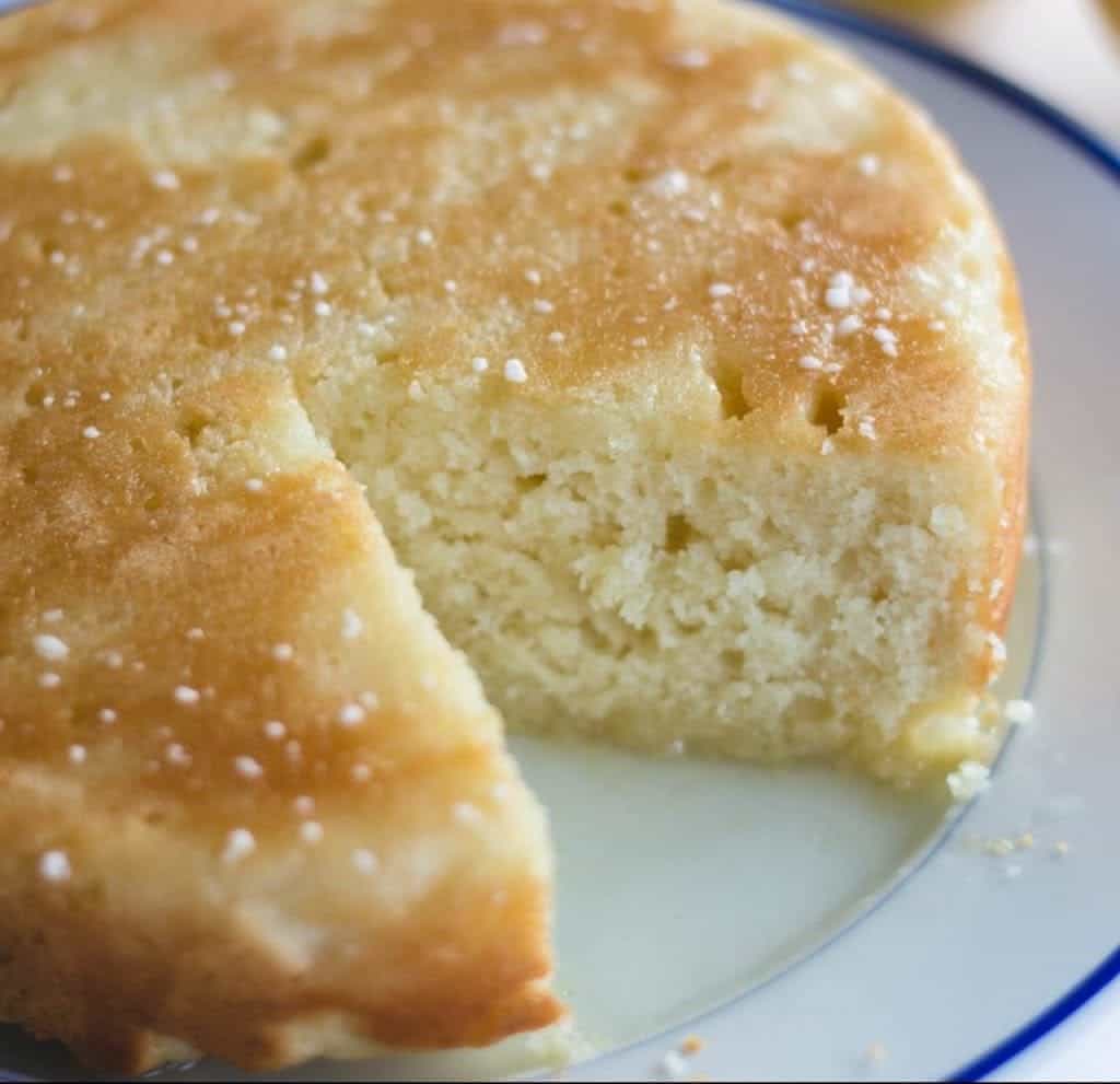 Single layer lemon coffee cake sprinkled with powdered sugar on blue rimmed plate.