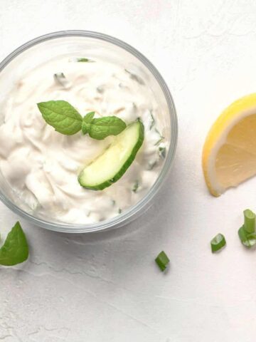 Fresh Greek tzatziki sauce in clear bowls on white table.