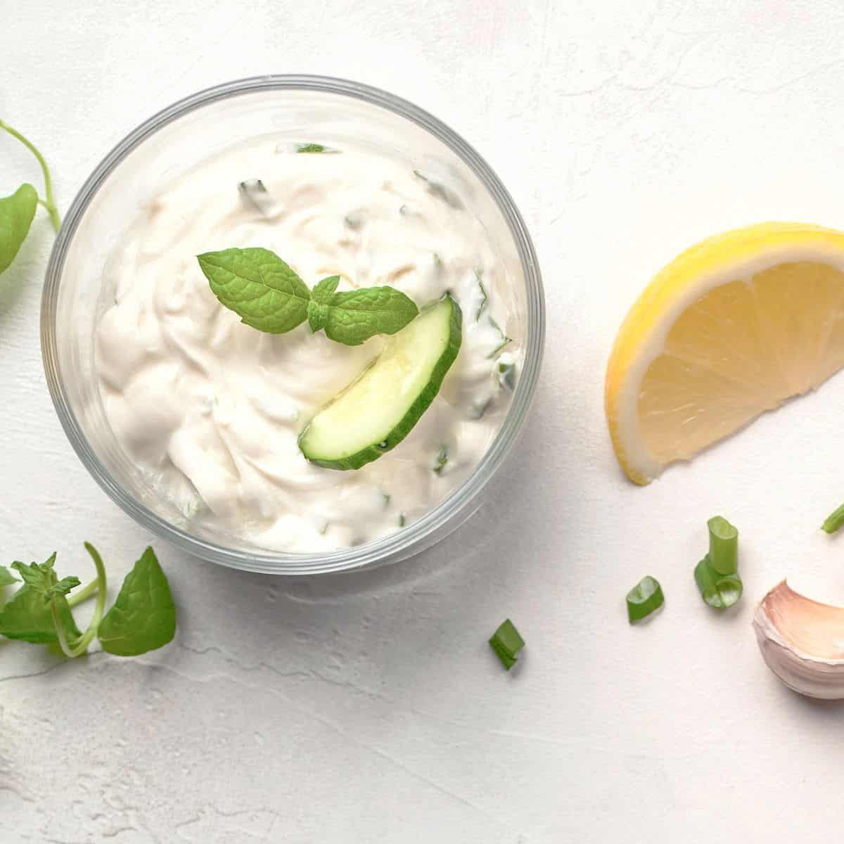 Fresh Greek tzatziki sauce in clear bowls on white table.