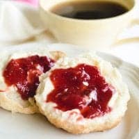 homemade biscuits topped with strawberry rhubarb jam on white plate.