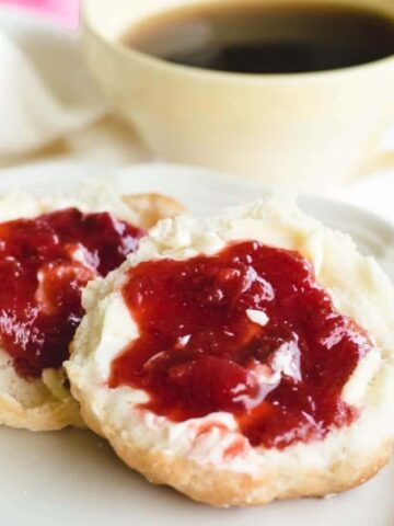 homemade biscuits topped with strawberry rhubarb jam on white plate.