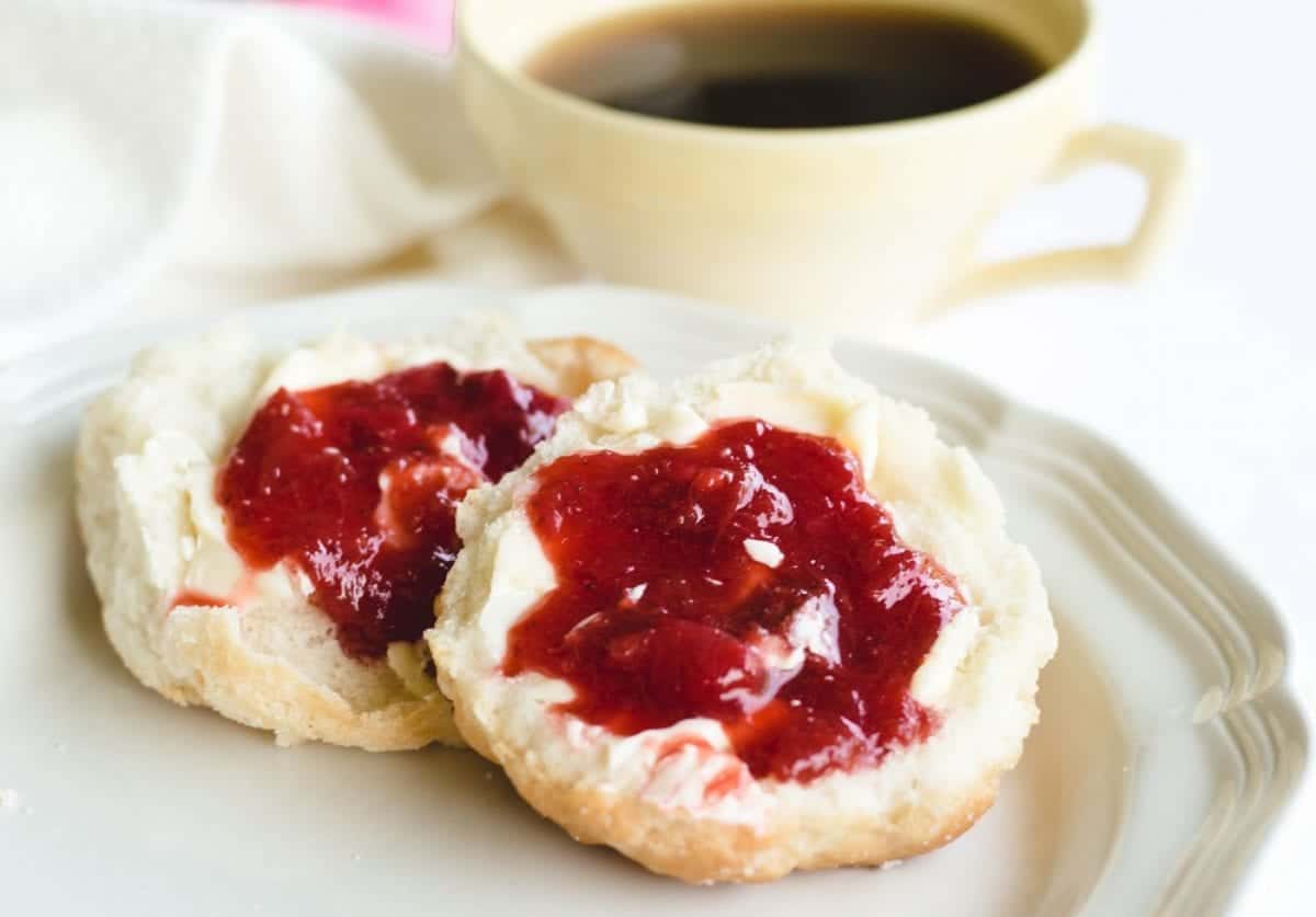 homemade biscuits topped with strawberry rhubarb jam on white plate.