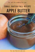 small mason jar filled with apple butter and whole apples on table.