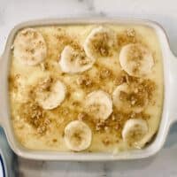 vanilla pudding in rectangular casserole dish topped with sliced bananas and graham cracker crumbs.