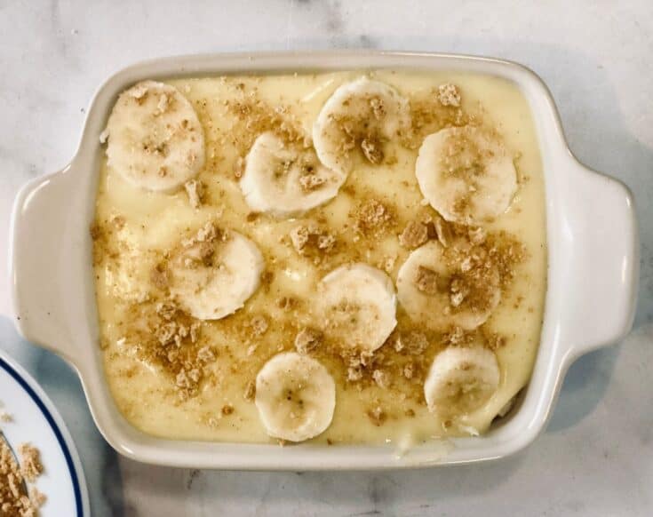 vanilla pudding in rectangular casserole dish topped with sliced bananas and graham cracker crumbs.