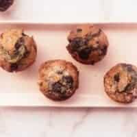four homemade blueberry muffins on pink rectangular plate.