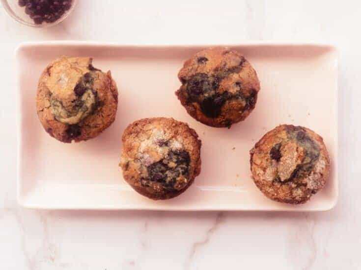 four homemade blueberry muffins on pink rectangular plate.