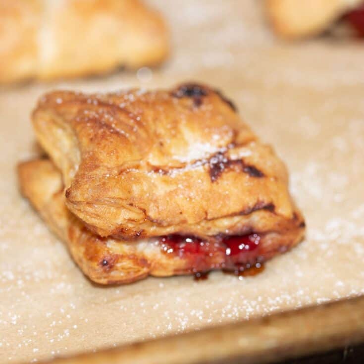 close up of cherry puff pastry cookie on parchment lined baking sheet.