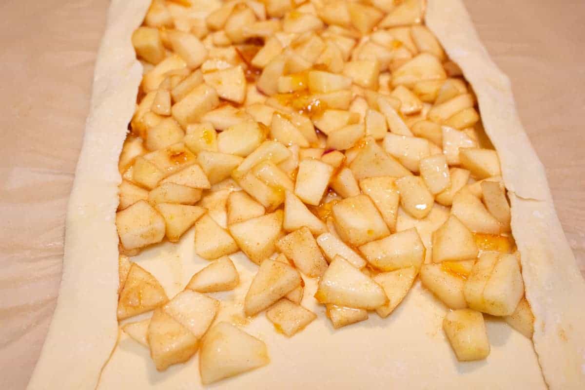 Chopped apples spread out on puff pastry sheet.
