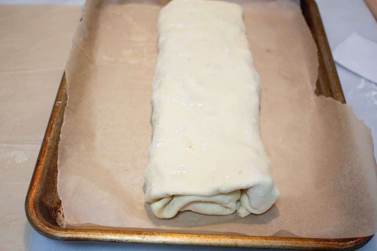 Unbaked apple strudel rolled up on parchment lined baking sheet.