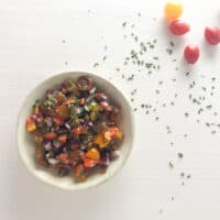 tomato relish in small bowl with cherry tomamtoes on board.