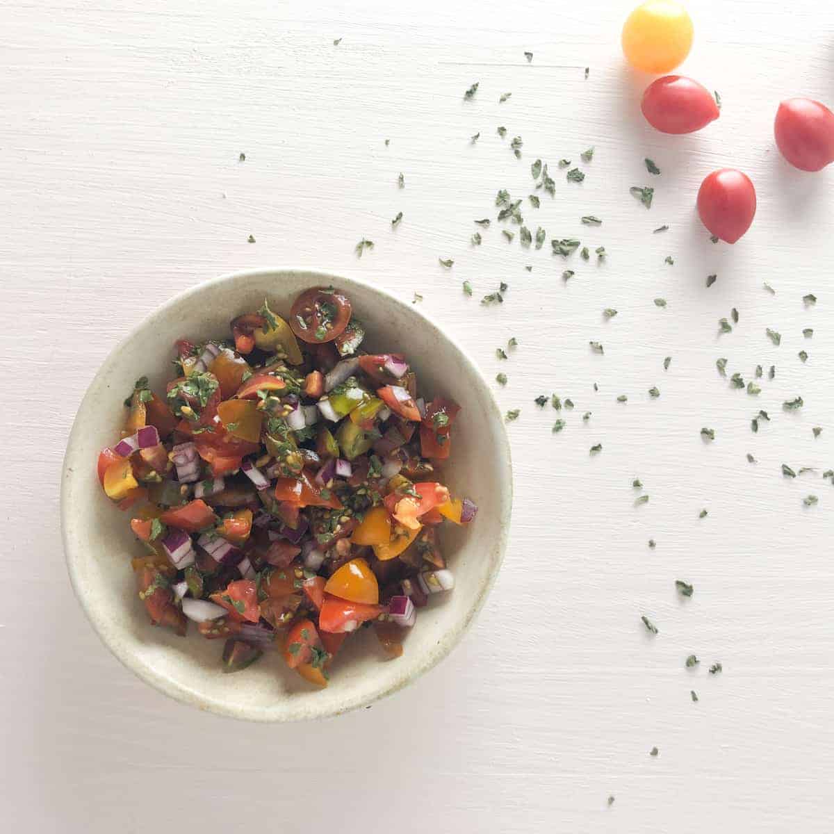 tomato relish in small bowl with cherry tomamtoes on board.