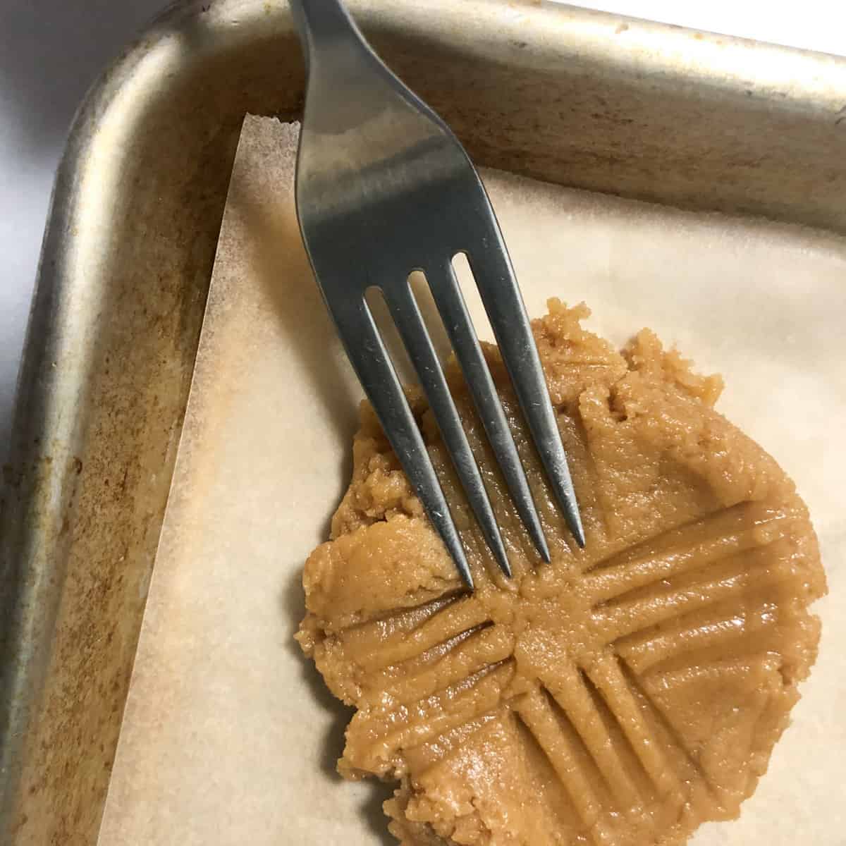 using tines of a fork to create a crisscross pattern on peanut butter cookie dough.
