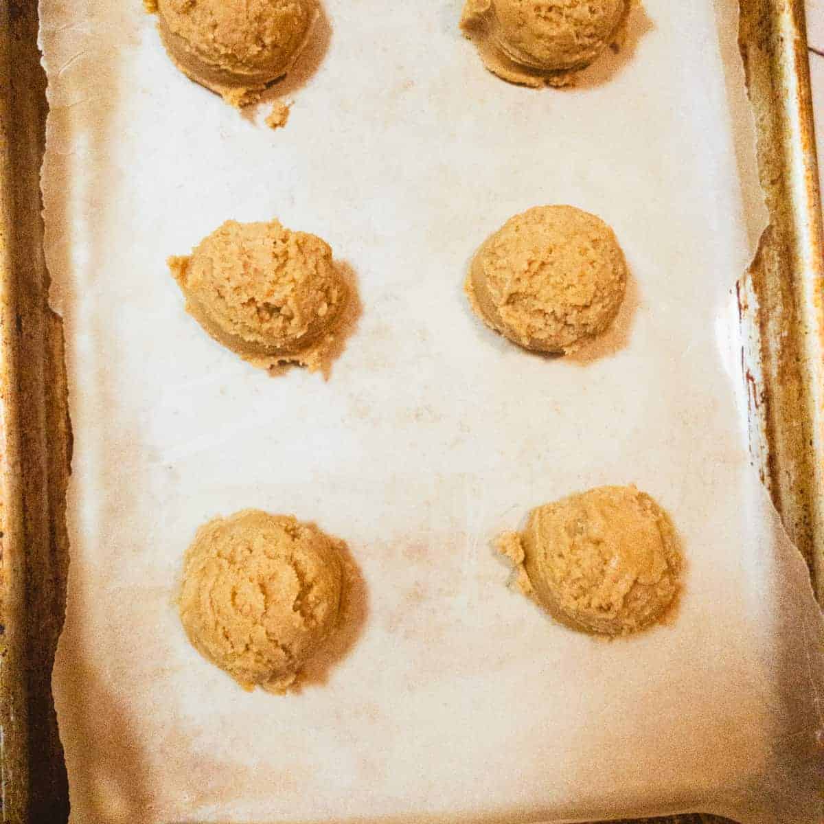 peanut butter cookie dough balls on parchment linedbaking sheet.