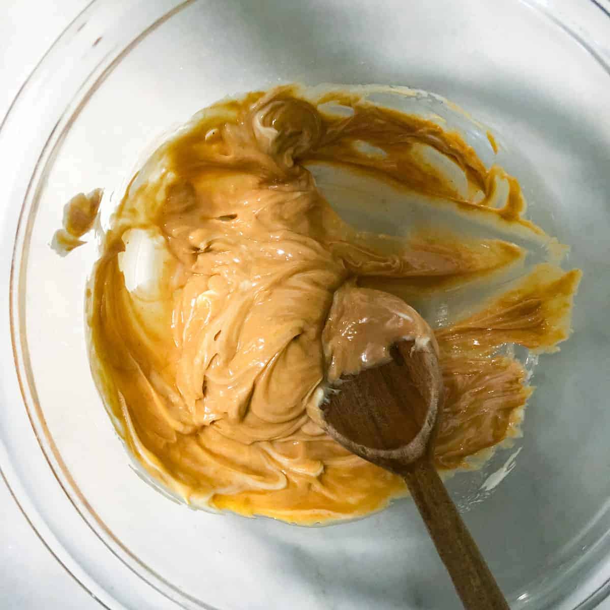 mixed peanut butter and butter in aclear bowl and wooden spoon.