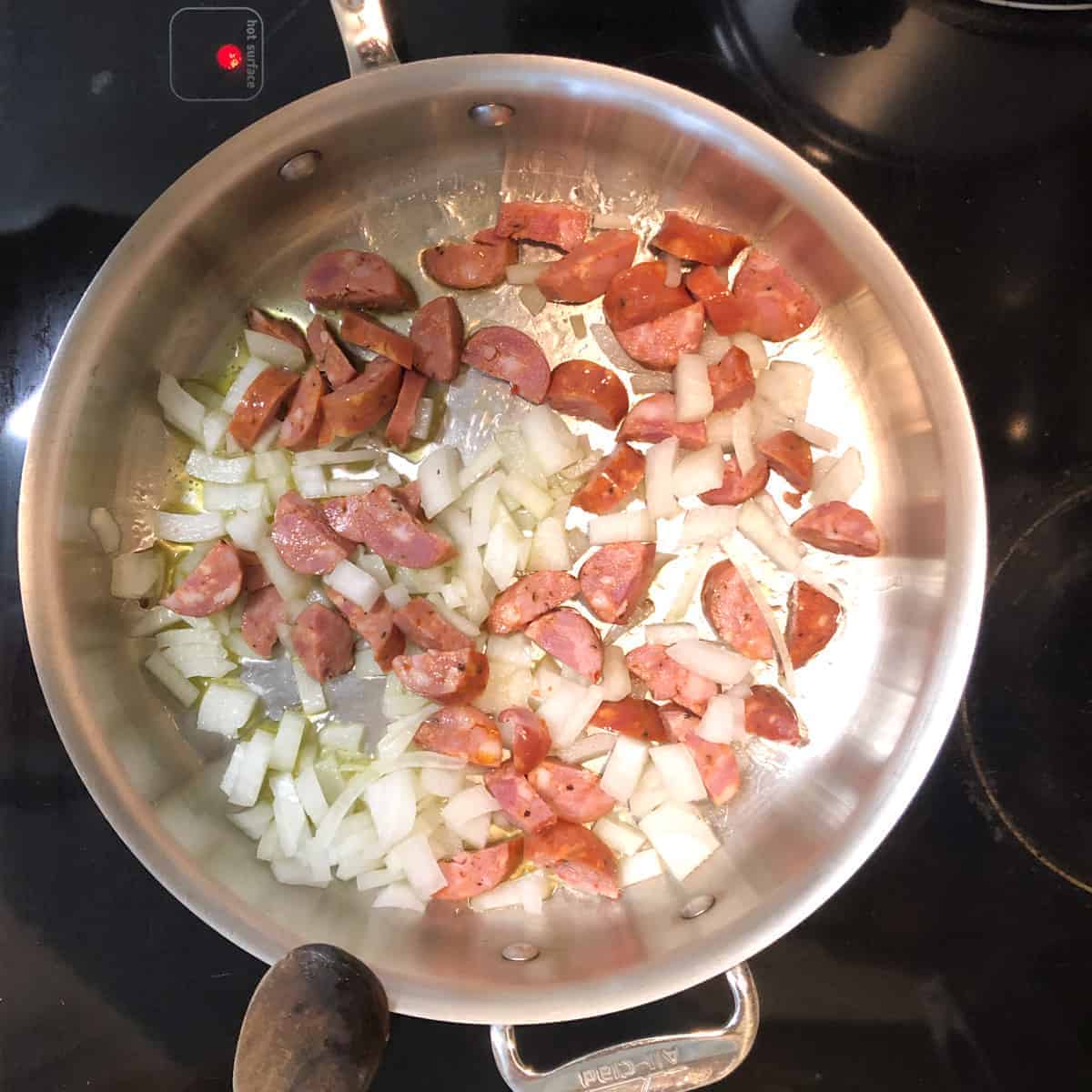 sausage and onions cooking in stainless stee skillet.