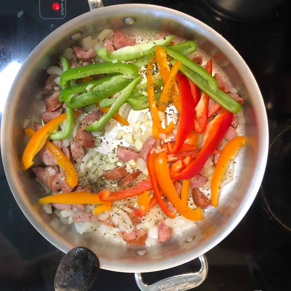 sausage onions, and bell peppers cooking in stainless stell skillet.