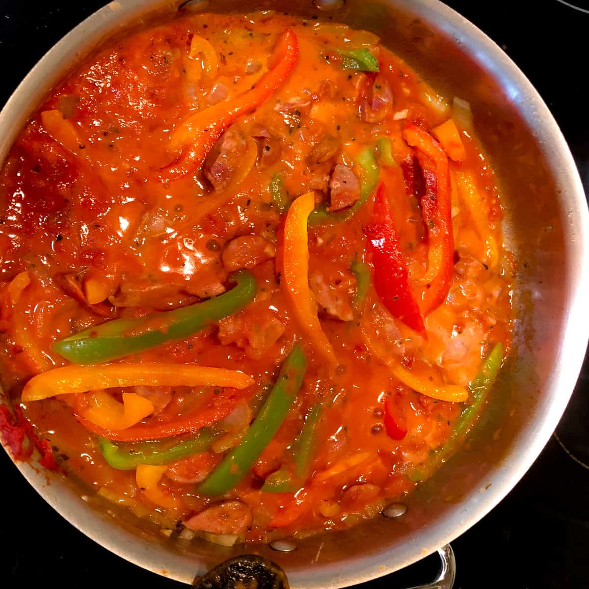 sausage and peppers in tomato sauce simmering in stainless stell skillet.