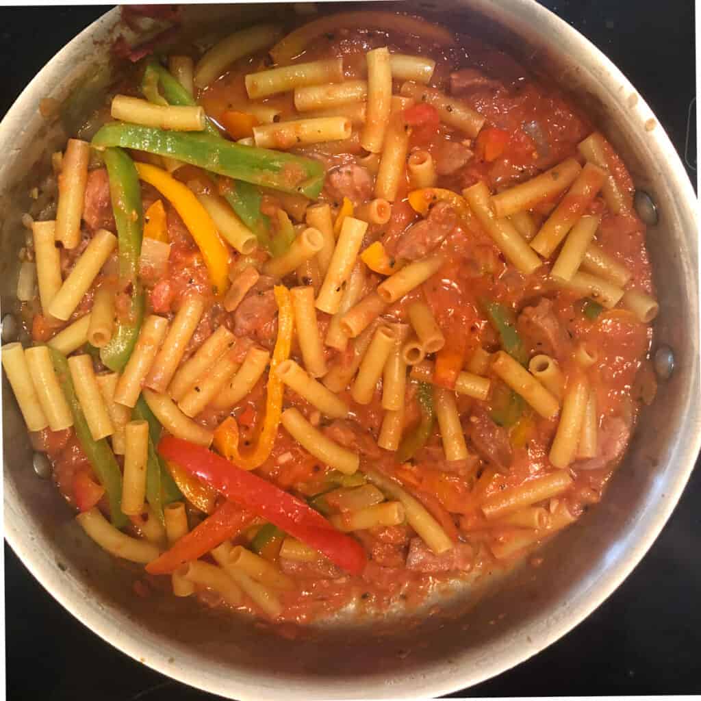 sausage, peppers, tomato saucem and ziti simmering in a stainless steel skillet.