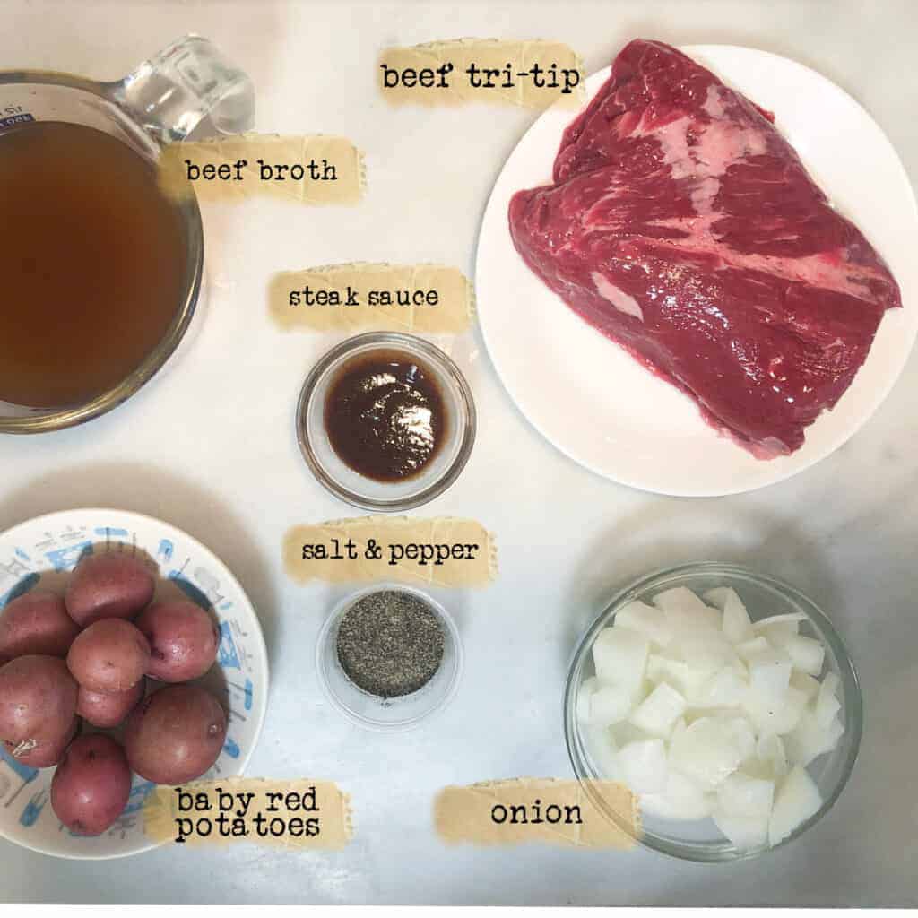 trip tip, potatoes, onion, steak sauce, seasoning and beef broth ingredients measured out on a marble board to make a one pound tri tip in a 3 quart slow cooker.