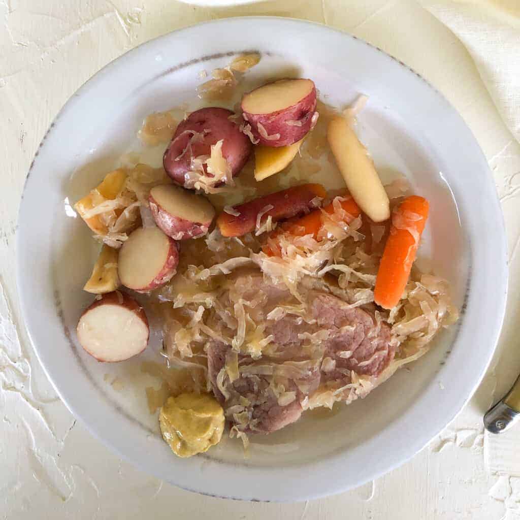 closeup overhead of ham steak and sauerkraut on rustic white plate.