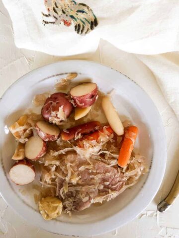 ham steak with sauerkraut and potatoes on rustic white plate.