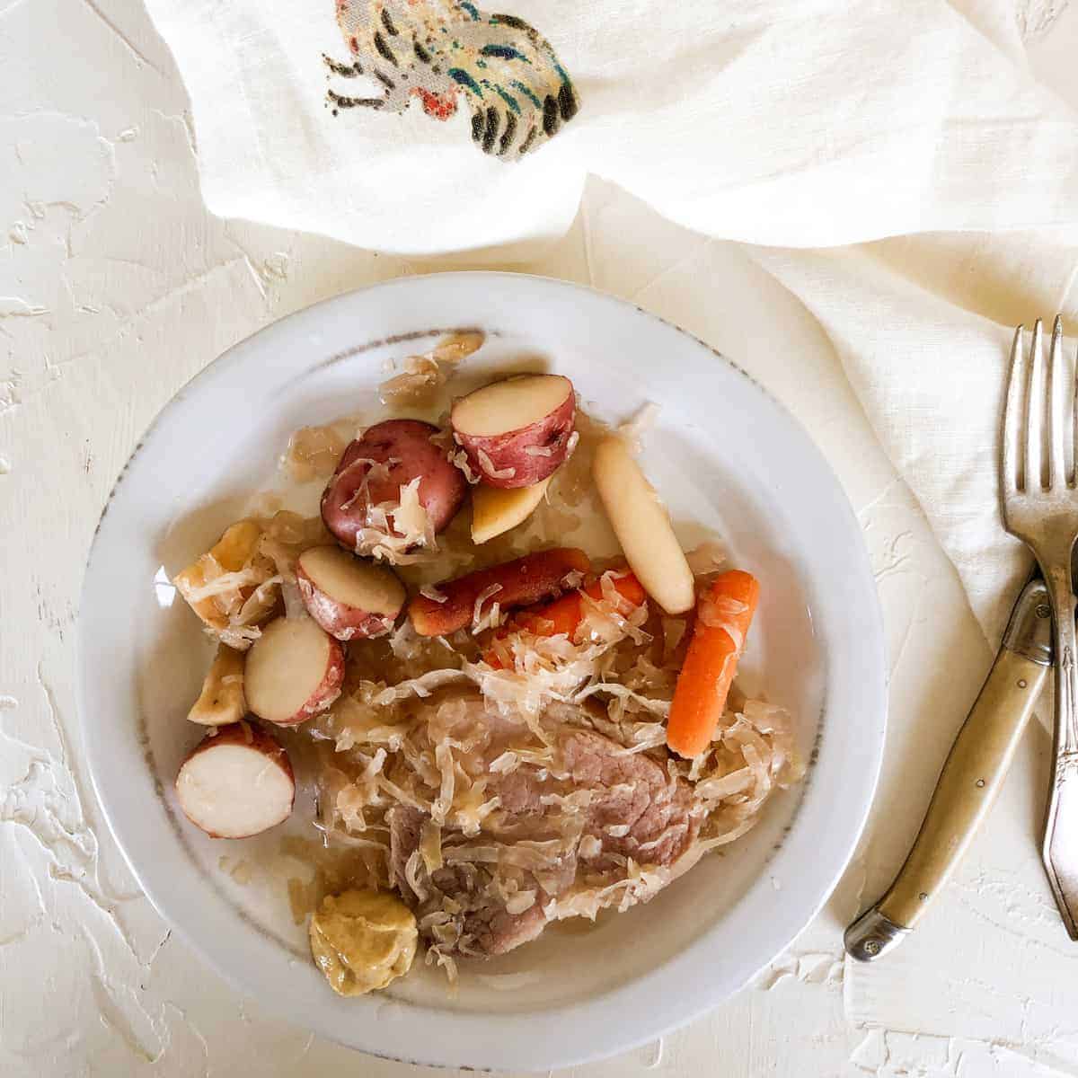 ham steak with sauerkraut and potatoes on rustic white plate.