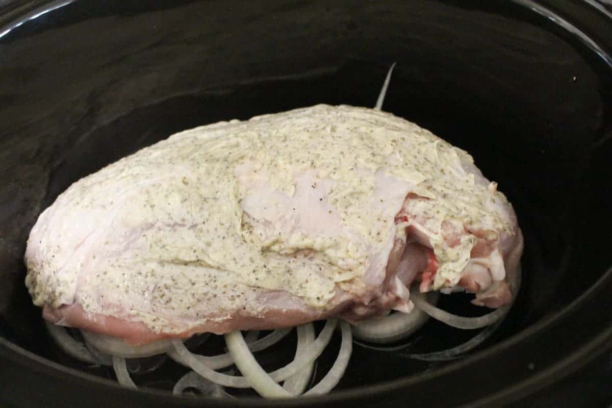 seasoned bone-in turkey breast on bed of onions in slow cooker.