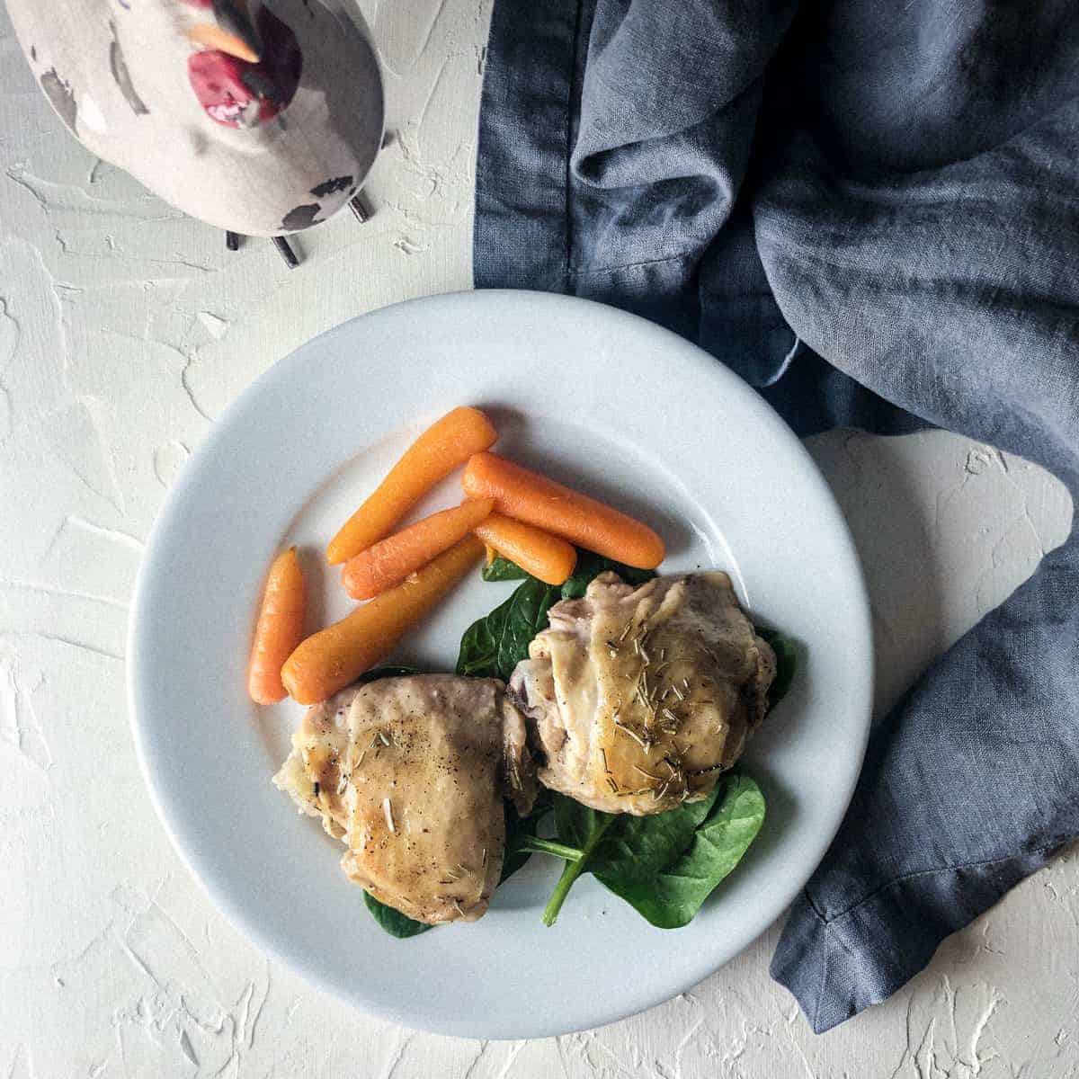 Plate of baby carrots and chicken thighs on bed of spinach,