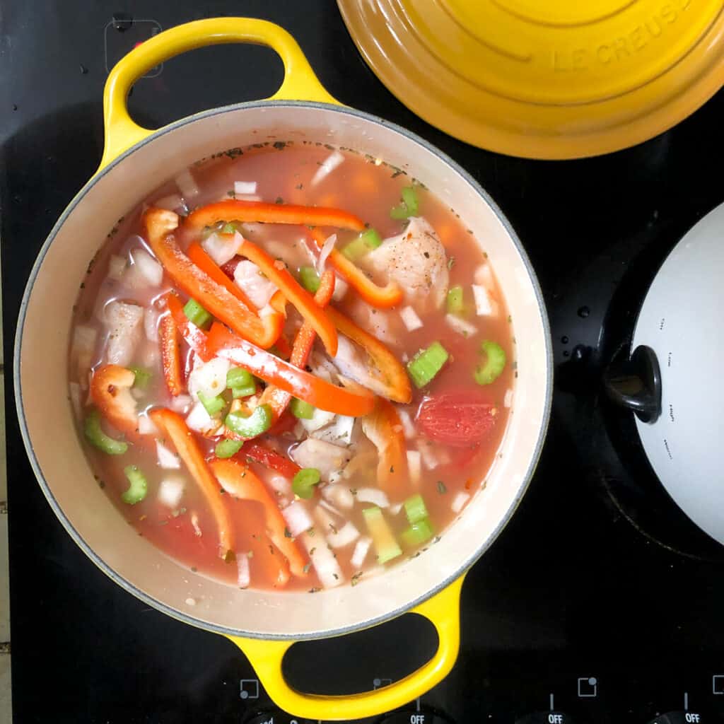 small chicken vegetable soup cooking in pLe Crueset pot on stovetop.