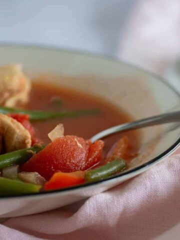 close up of bowl of chicken vegetable soup on pink linen napkin.