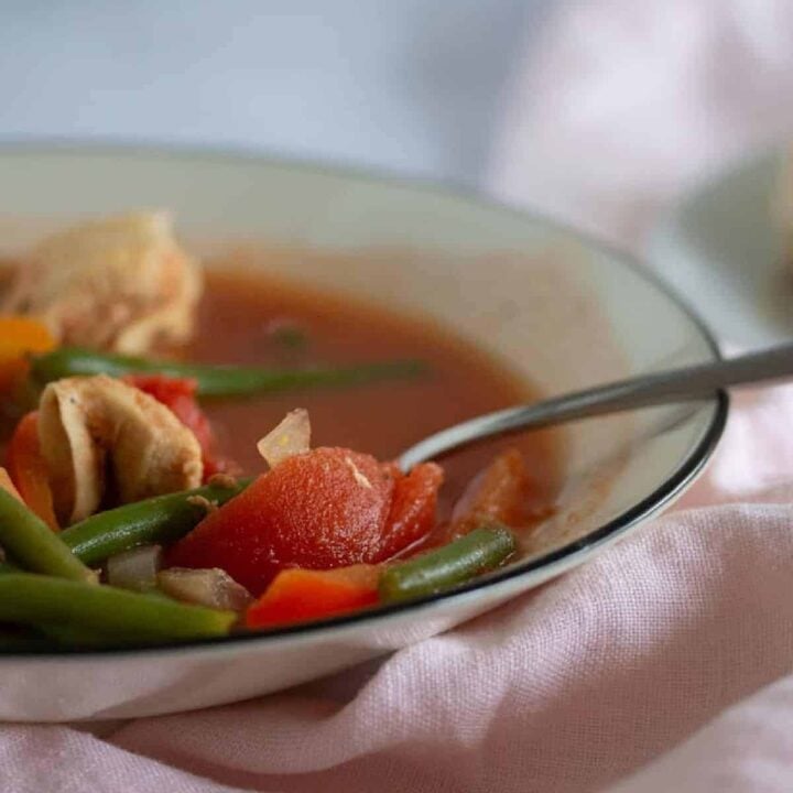 close up of bowl of chicken vegetable soup on pink linen napkin.