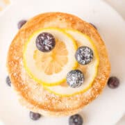 A stack of pancakes for one topped with lemon slices, blueberries, and powdered sugar on a white plate.