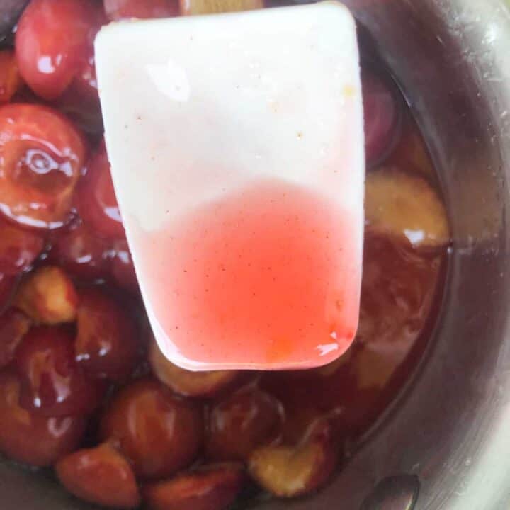 Cherries cooking in small saucepan with mini spatula.