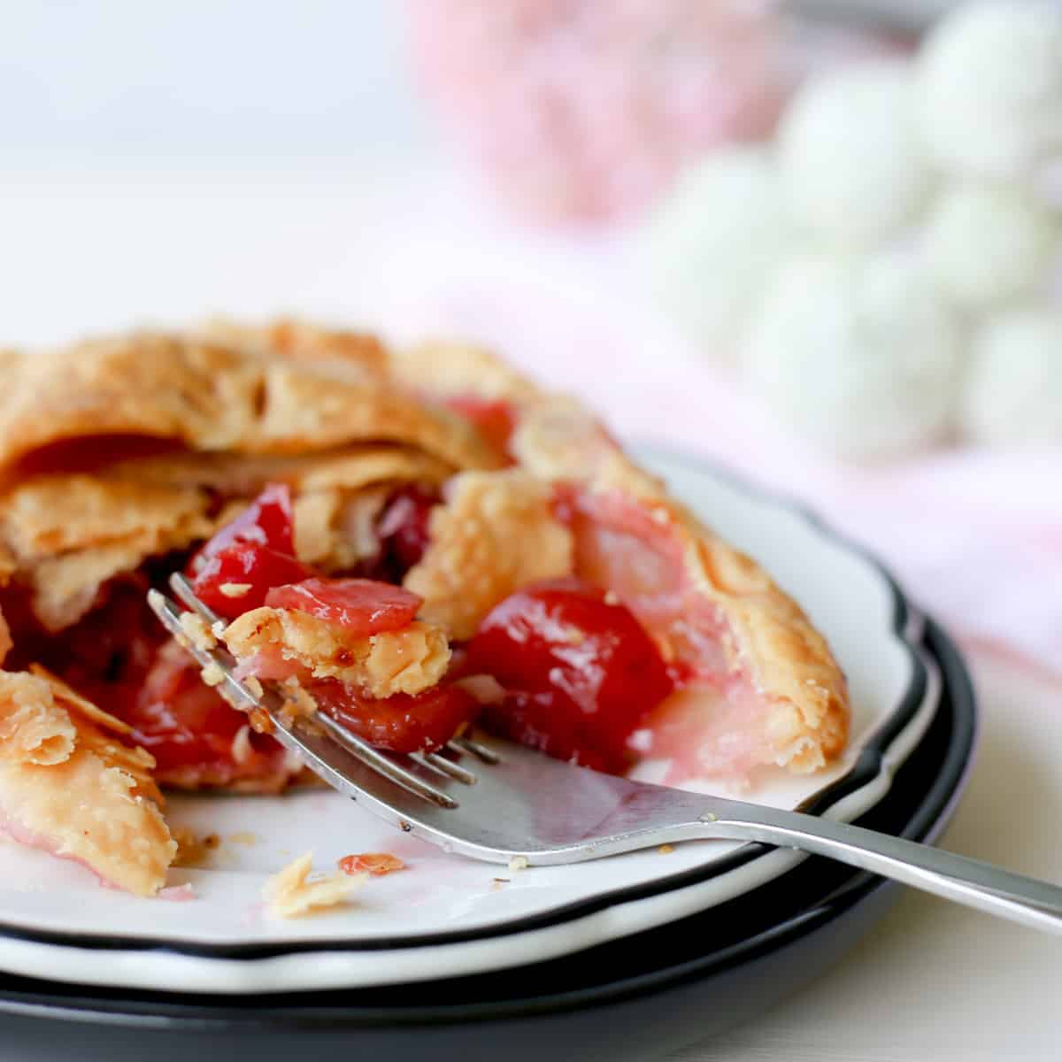 mini cherry pie on black rimmed plate with fork.