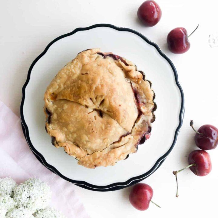 Overhead of a small cherry pie surrounded by fresh cherries.