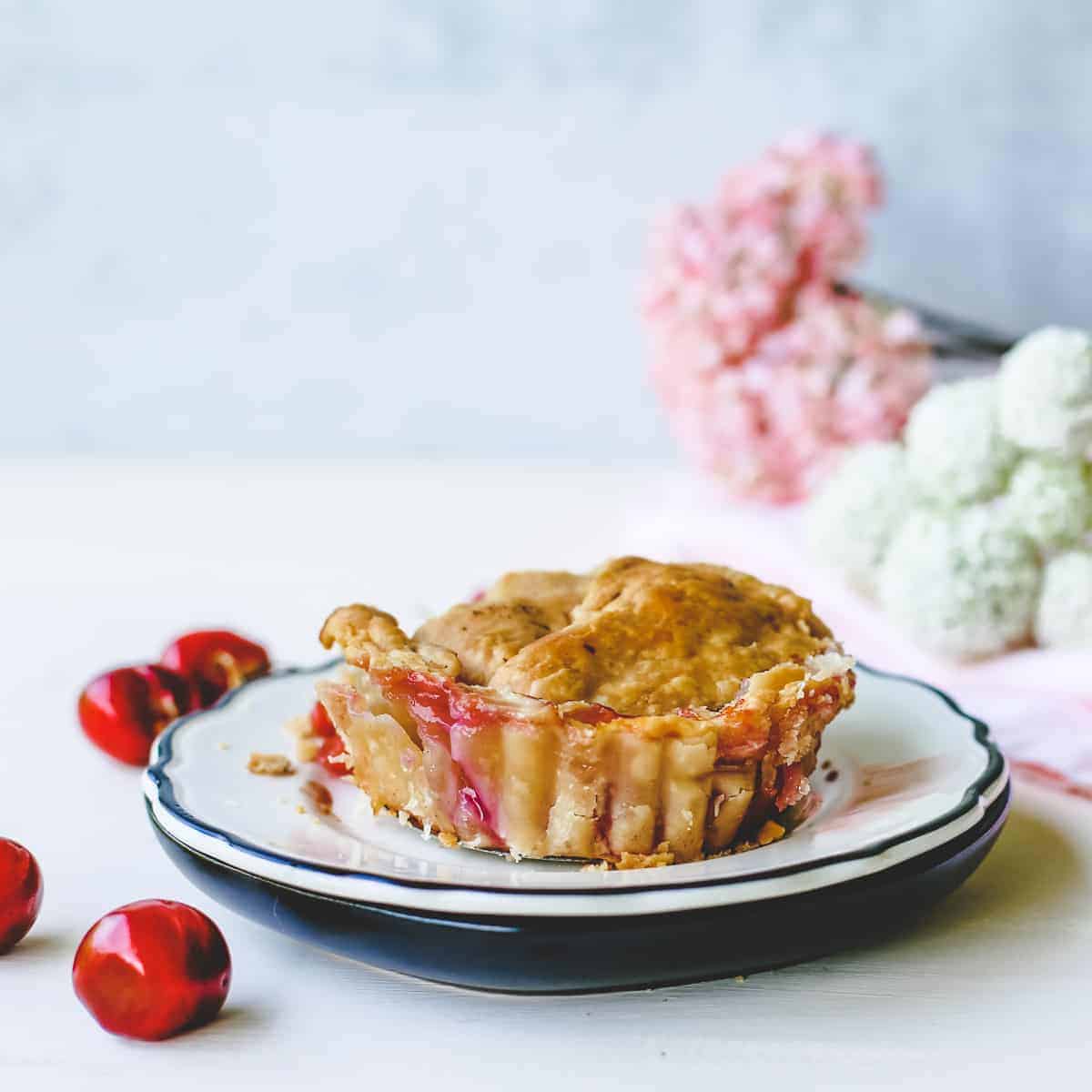 Mini cherry pie on plate with fresh cherries scattered on table."