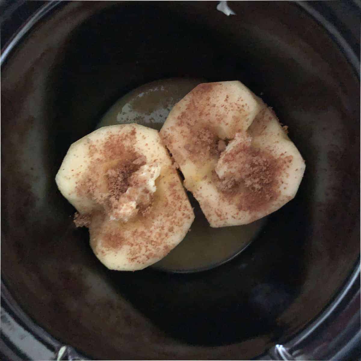 Peeled apple sliced in half sprinkled with butter and cinnamon is small crockpot.