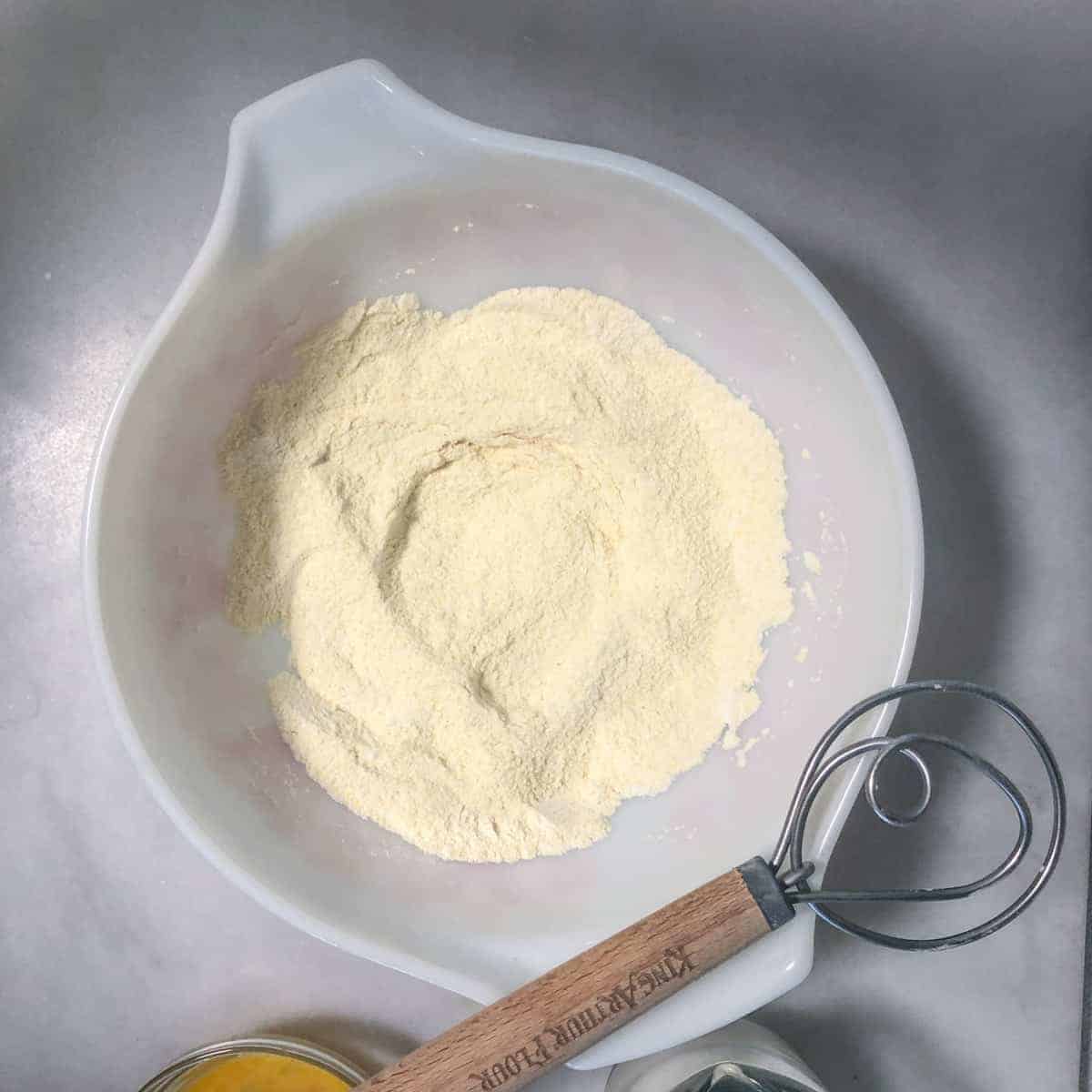 Bowl of cornmeal and flour with whisk.