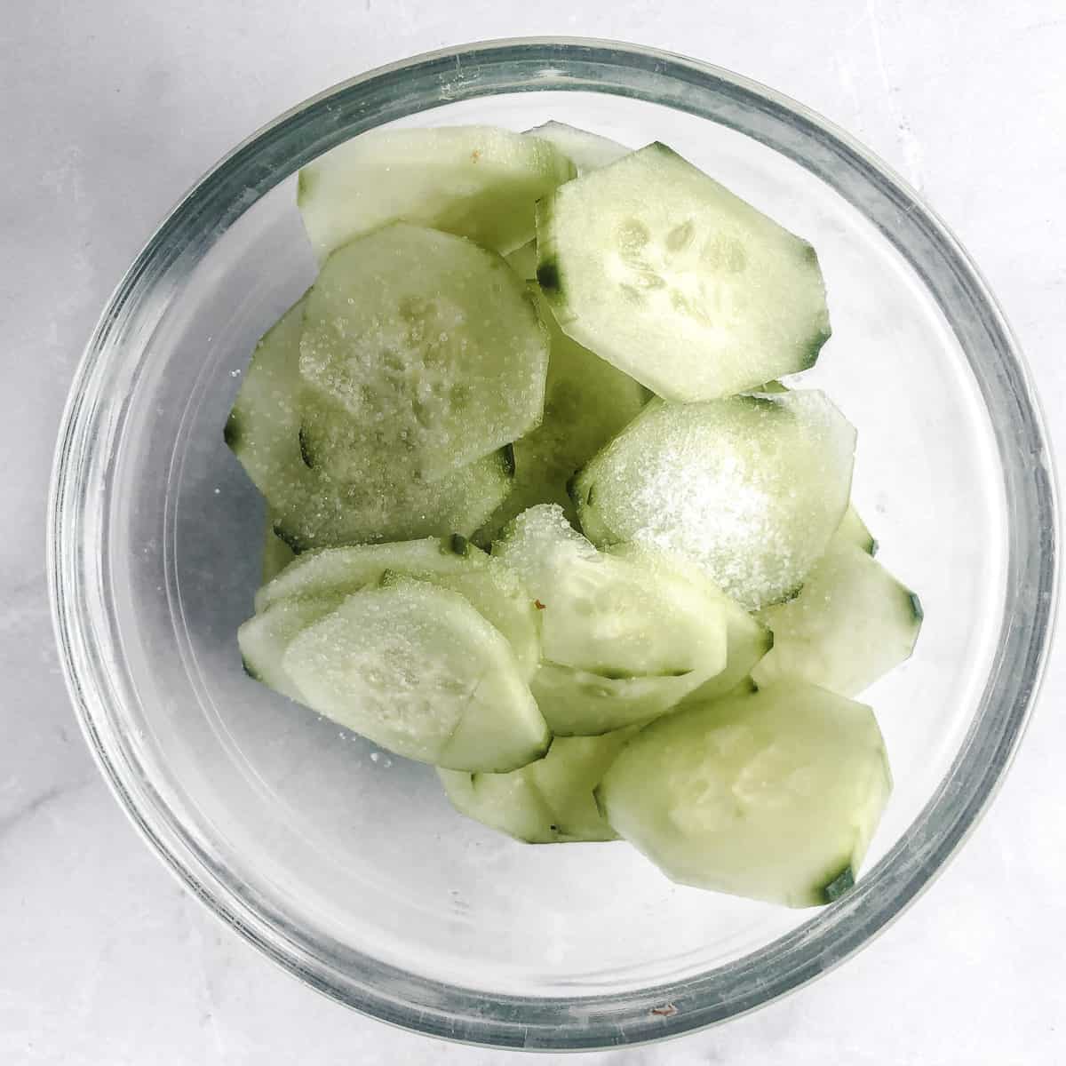 Bowl of thinly sliced cucumbers sprinkled with salt.