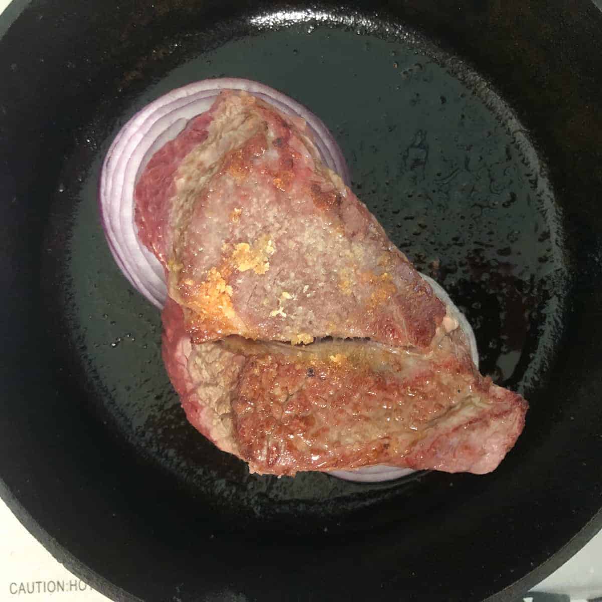 Pot roast on bed on onions in cast iron skillet.