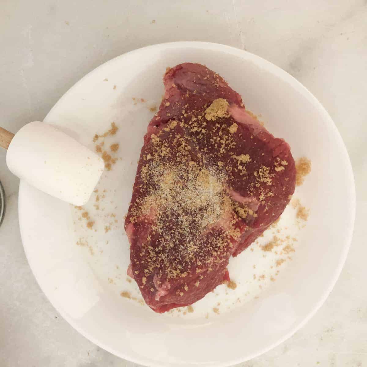 Piece of beef seasoned on white plate.