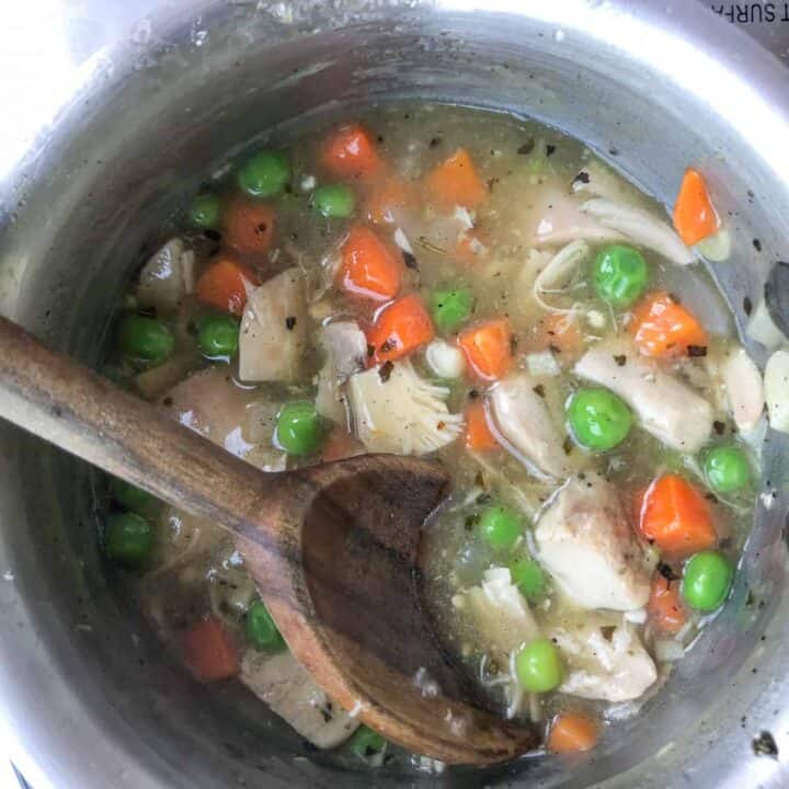 Chicken, carrot and peas simmering in saucepan.
