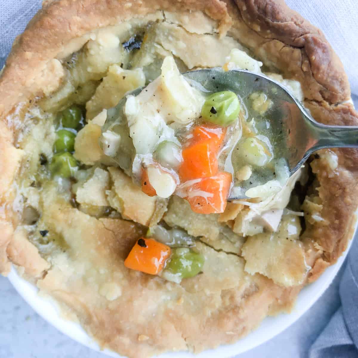 Chicken pot pie filling on spoon over baked pie.