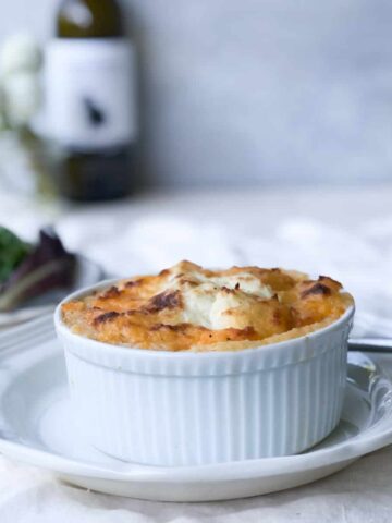 Serving of cottage pie with salad, wine and flowers in background.