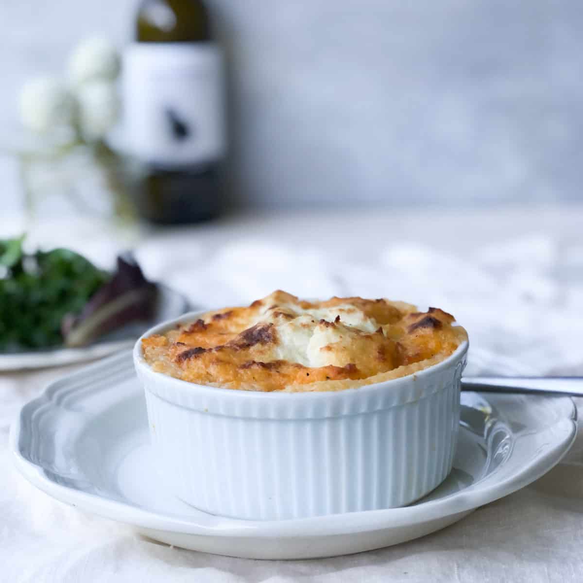 Serving of cottage pie with salad, wine and flowers in background.