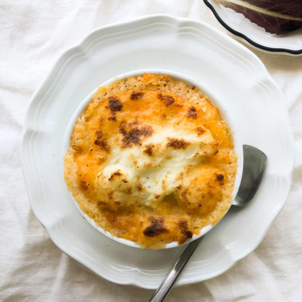 Overhead view of baked cottage pie in round baking dish on plate.
