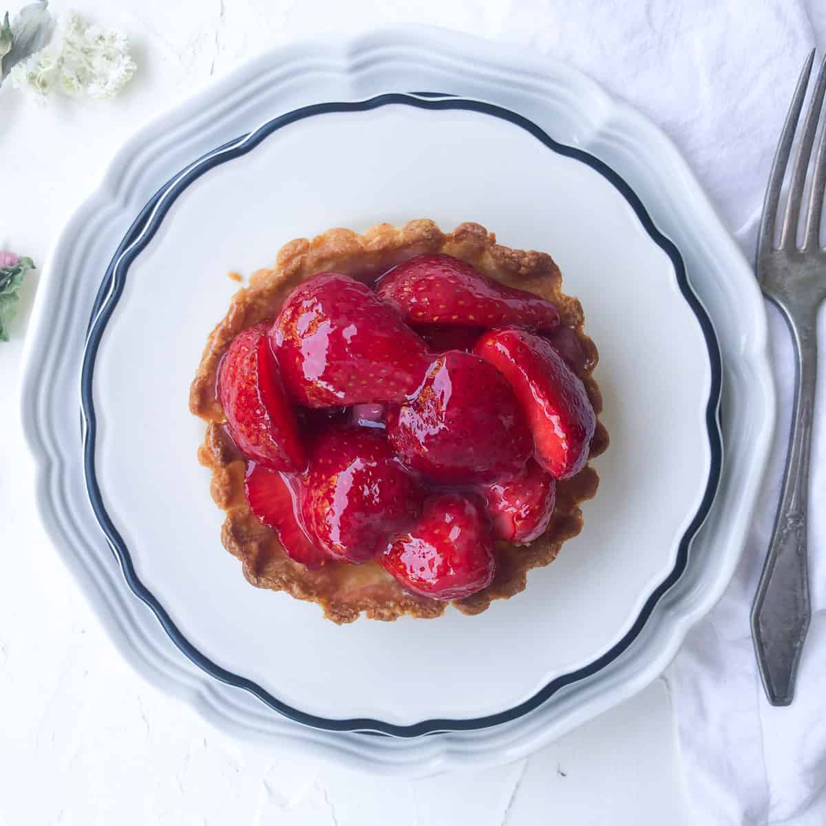 Overhead view of strawberry pie on plate with scattered dried flowers on table.