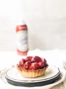 A mini strawberry pie on plate with can of whipped cream behind it.