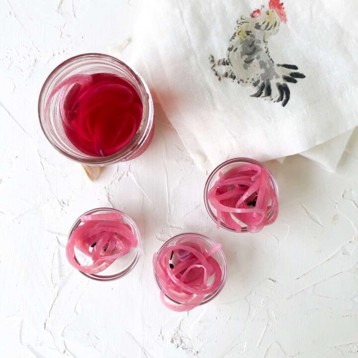 Three small bowl and canning jar filled with quick pickled red onions.